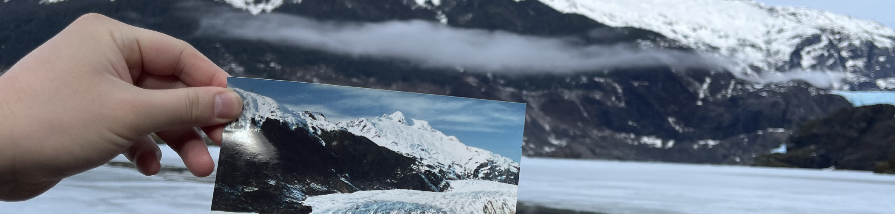 Someone holds an older photo of an Alaskan glacier to the current state of the glacier to show its degradation