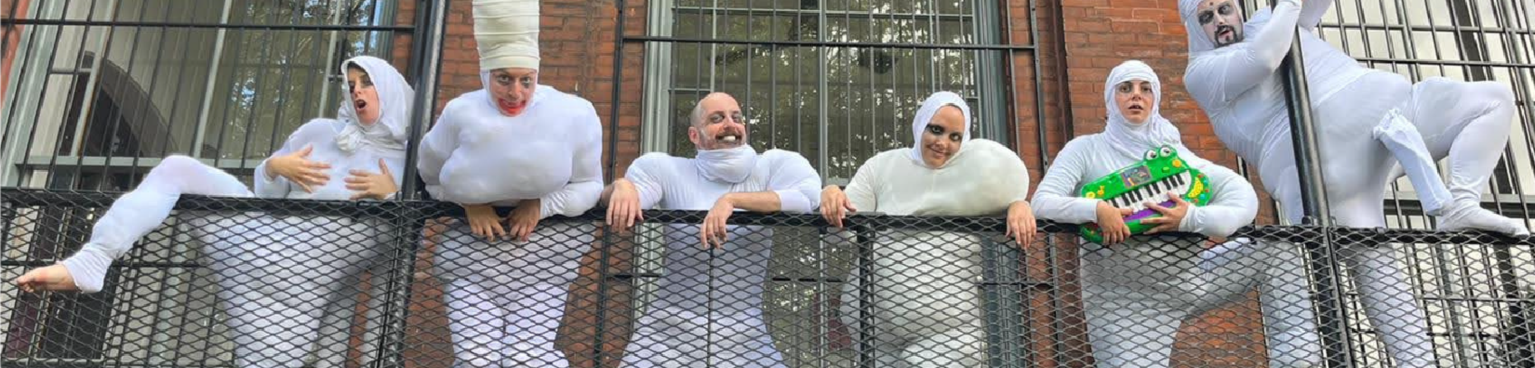 Actors in white costumes stand on a fire escape in various humorous poses